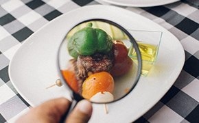 Image shows a plate of food components under a magnifying glass on top of a black and white checkered cloth